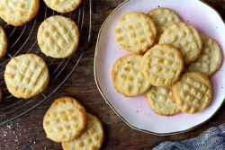 Small pale cookies scattered across a white plate and a wooden tabletop surface